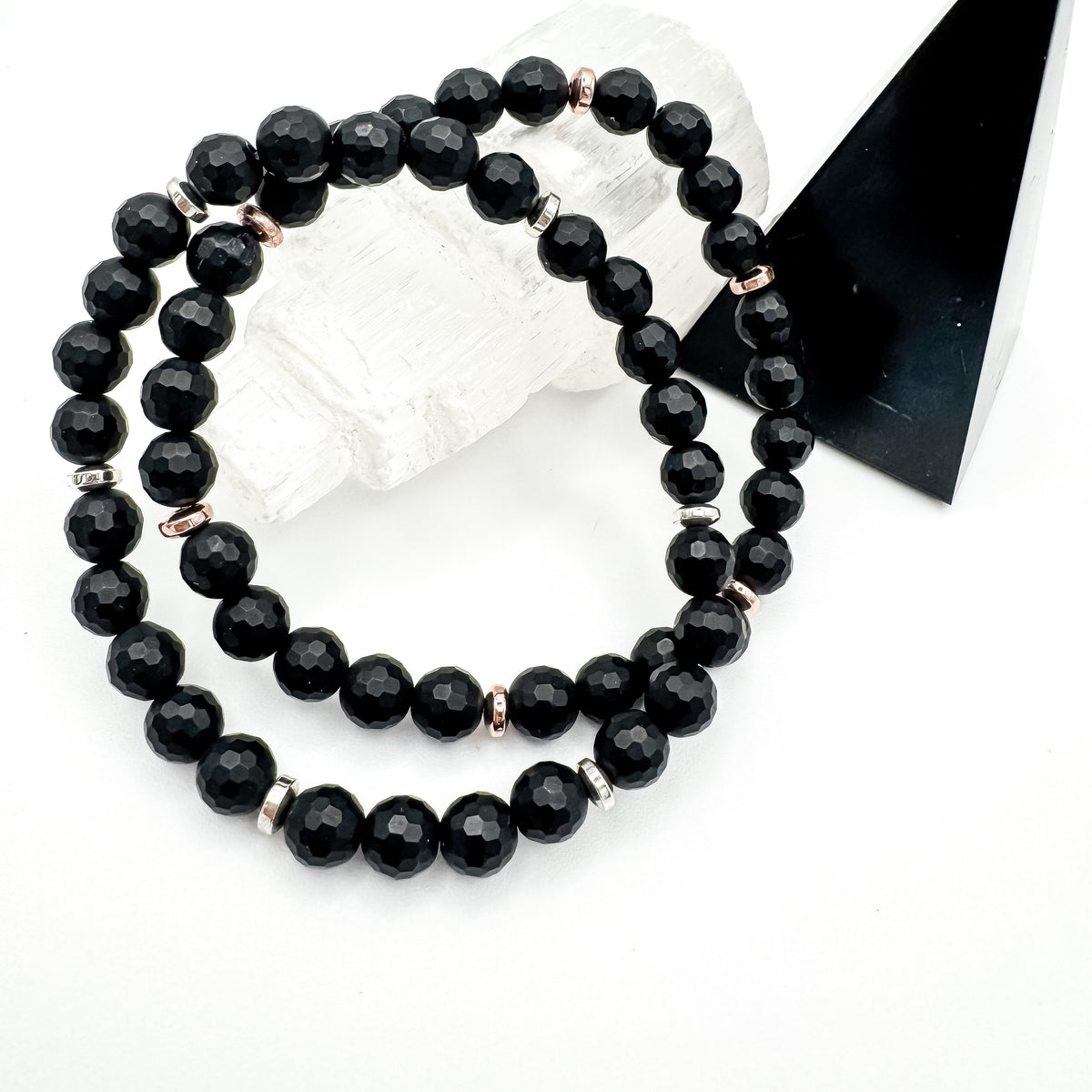 Faceted matte black onyx and hematite handmade bracelet pair with 6mm black onyx beads and silver and rose gold hematite spacers resting on raw selenite crystal beside black pyramid, minimalist women's gemstone jewelry by Blue Jeans and Pearls Saskatchewan