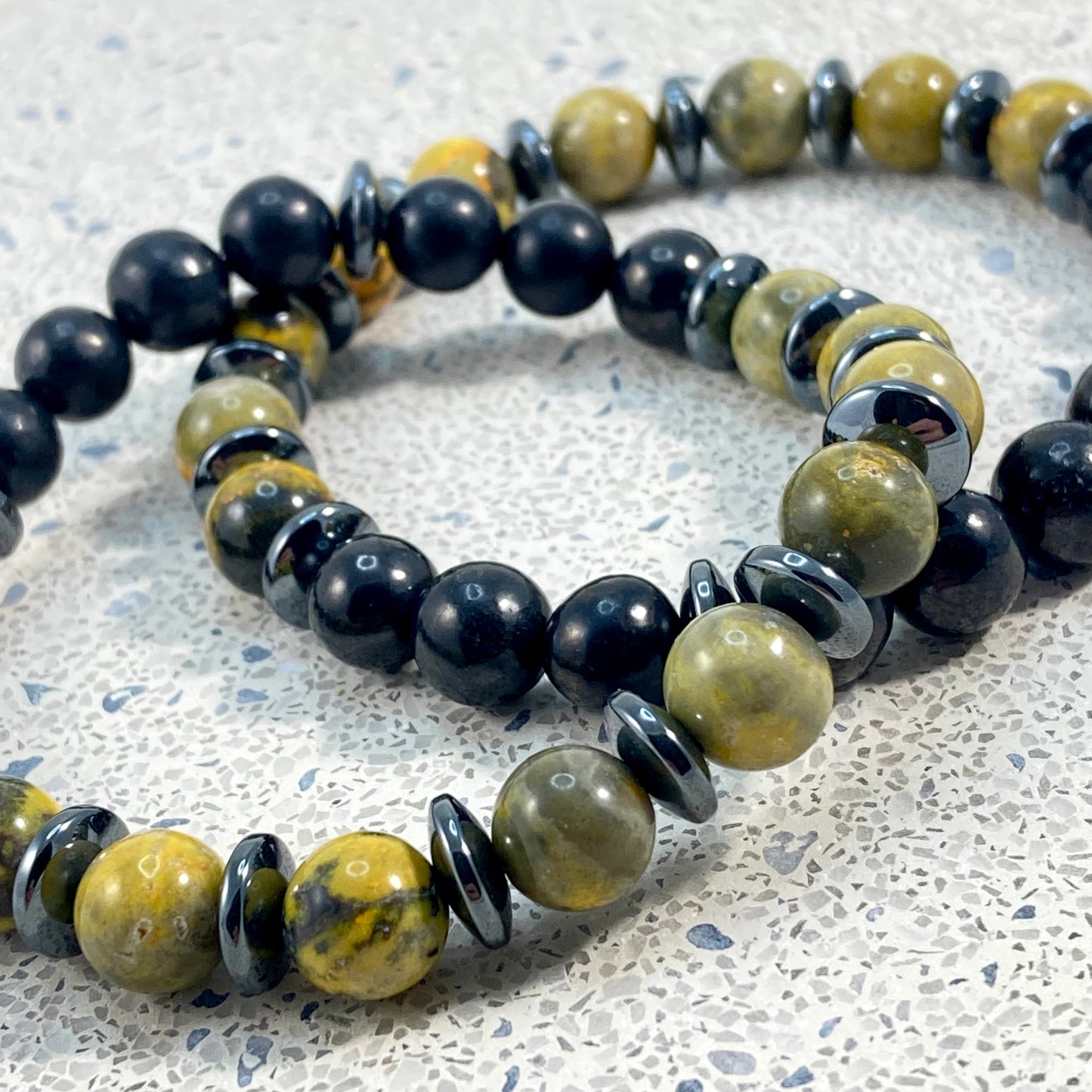 Men's Bumblebee Jasper, Shungite and Hematite handmade bracelet pair close up showing natural yellow and black jasper markings, polished shungite beads and glossy hematite spacers on terrazzo, men's crystal jewelry by Blue Jeans and Pearls Saskatchewan