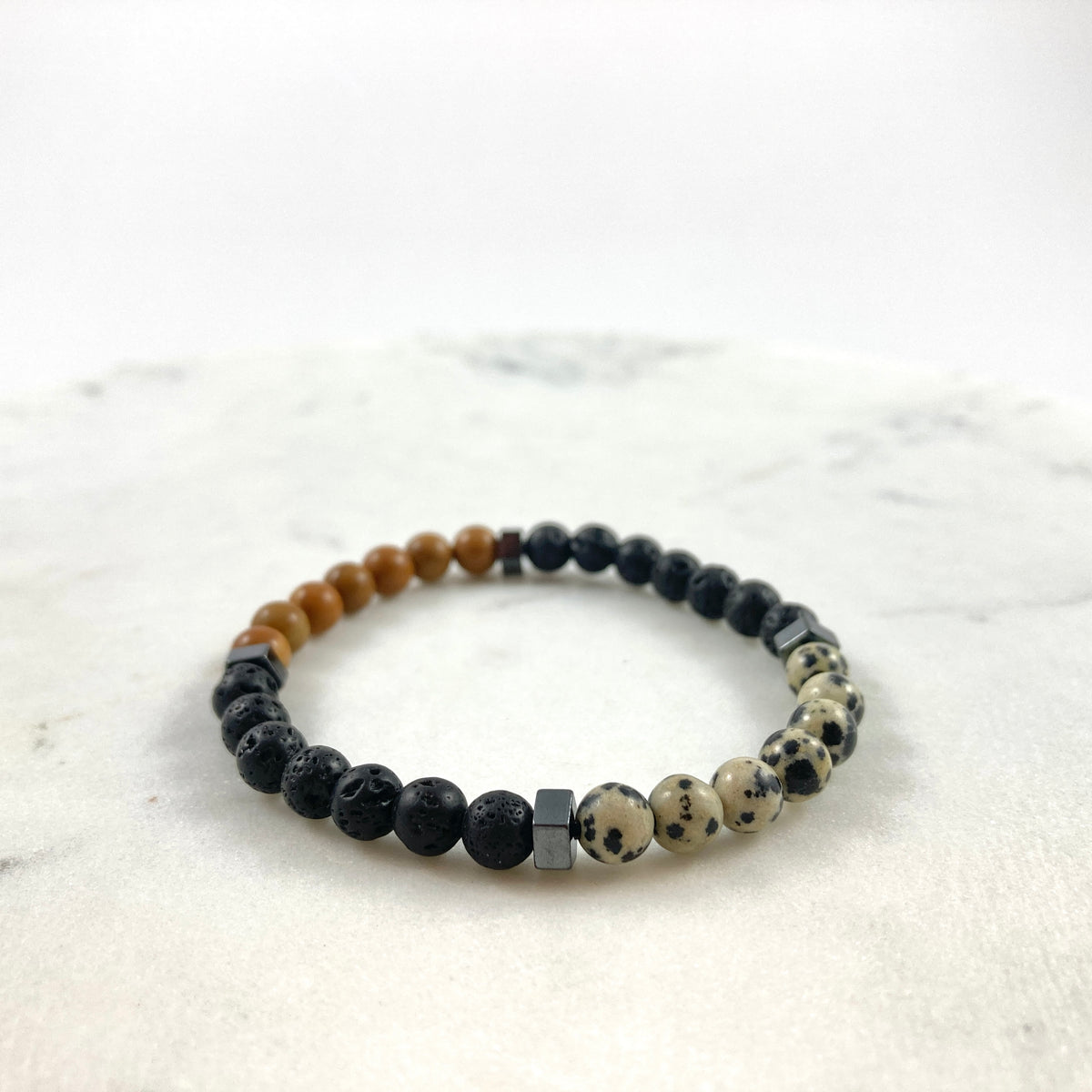 Men's handmade wood jasper, dalmatian jasper, lava stone and hematite cube bracelet showing natural stone sections on marble, grounding essential oil diffuser jewelry by Blue Jeans and Pearls Regina Saskatchewan