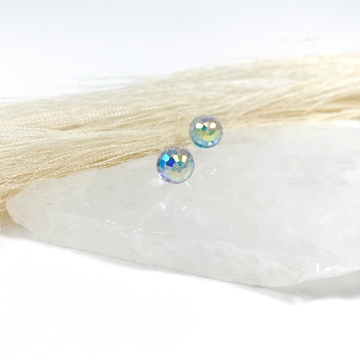 Aurora Borealis disco stud earrings pair with 8mm faceted Austrian crystal showing blue and gold rainbow flashes on raw white crystal with soft cream fringe, lightweight sparkly earrings for sensitive ears by Blue Jeans and Pearls Saskatchewan