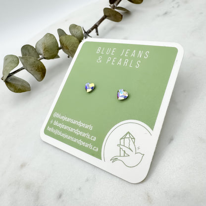 Aurora borealis Austrian crystal heart stud earrings displayed flat on a sage green Blue Jeans and Pearls earring card with eucalyptus sprig on white marble, tiny everyday studs with plastic posts for sensitive ears, Saskatchewan