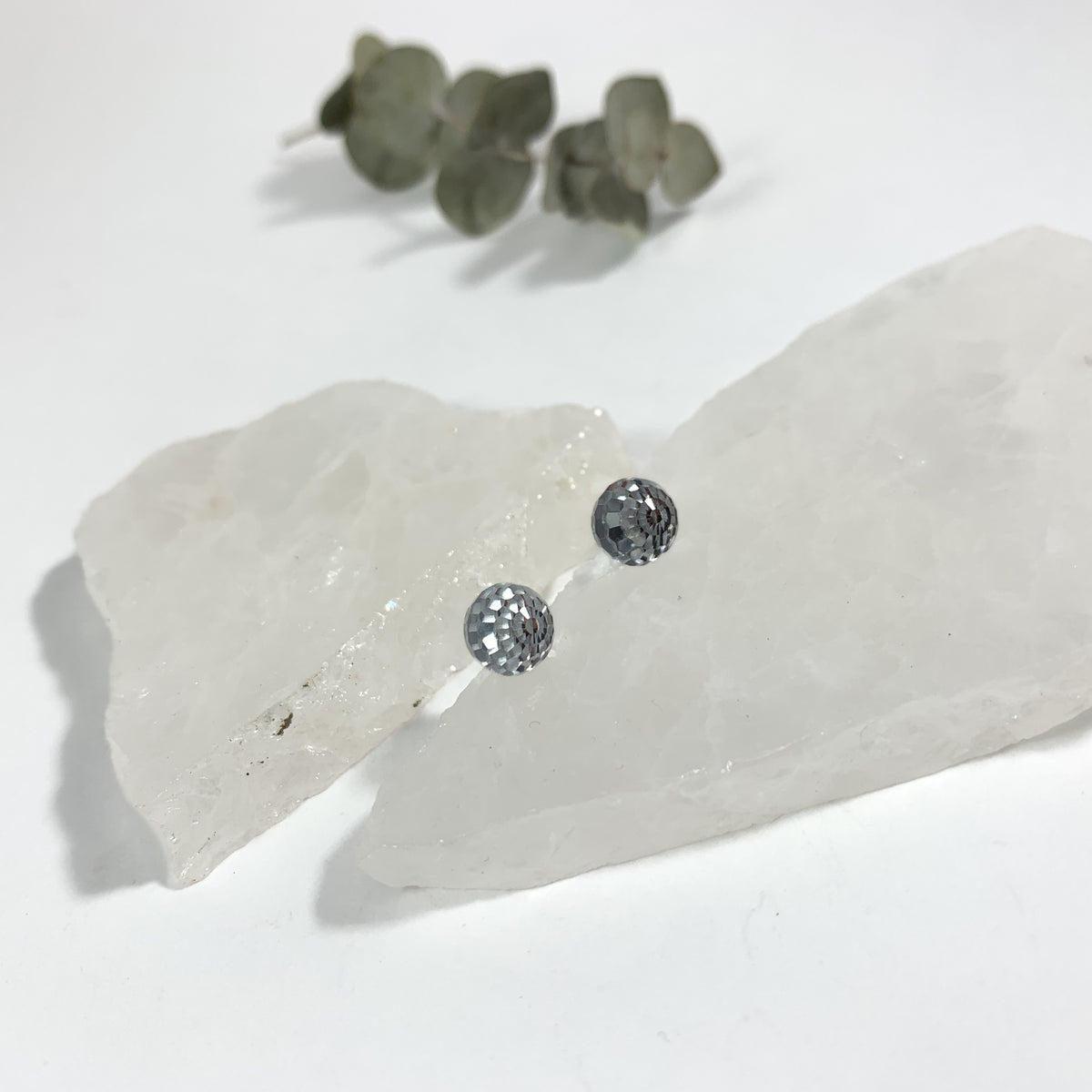 Crystal Clear disco stud earrings close up showing 8mm faceted Austrian crystal detail tucked between raw white crystal slabs with eucalyptus, sparkly hypoallergenic stud earrings for sensitive ears by Blue Jeans and Pearls Saskatchewan