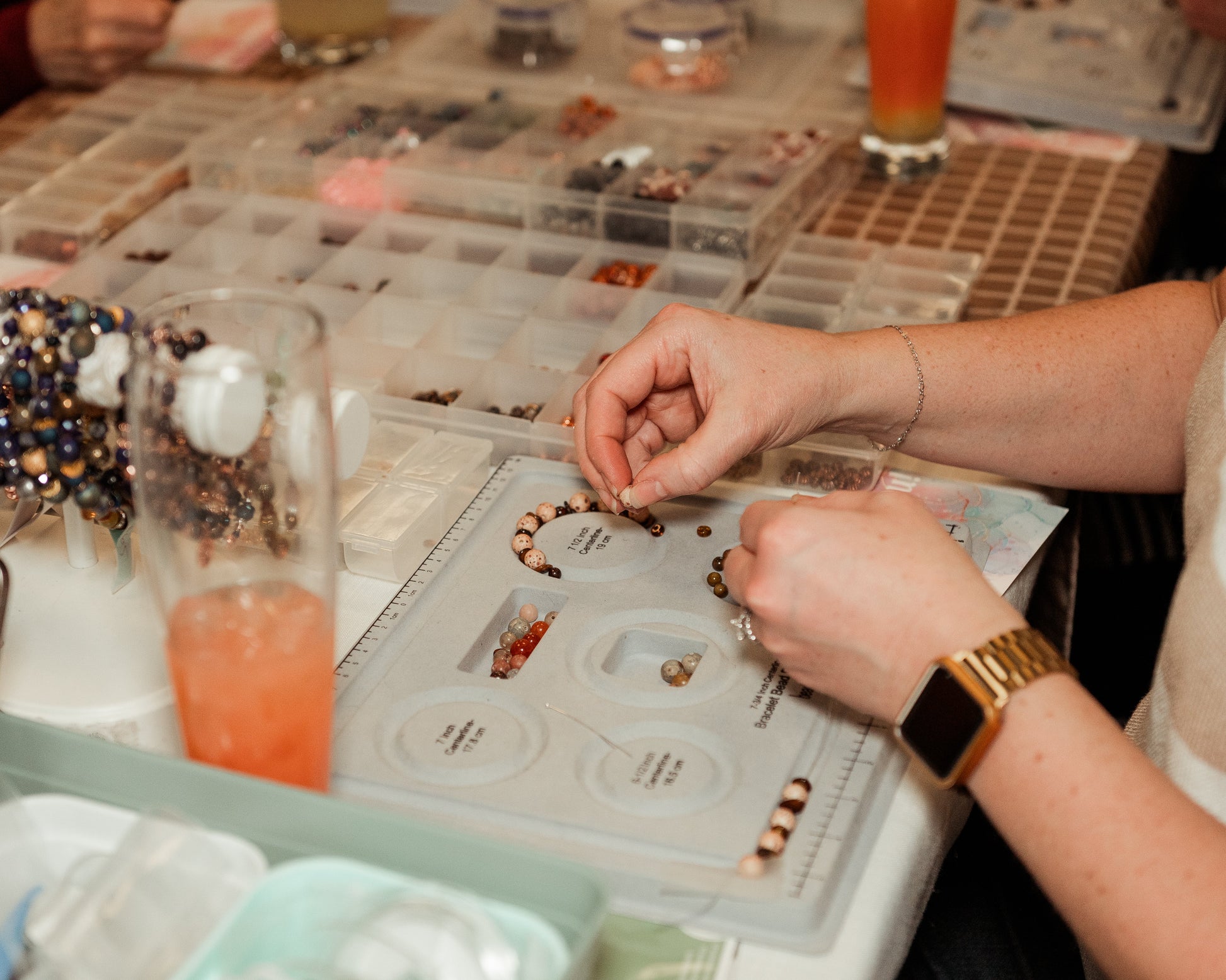 Person assembling jewelry at a table with various supplies and tools.