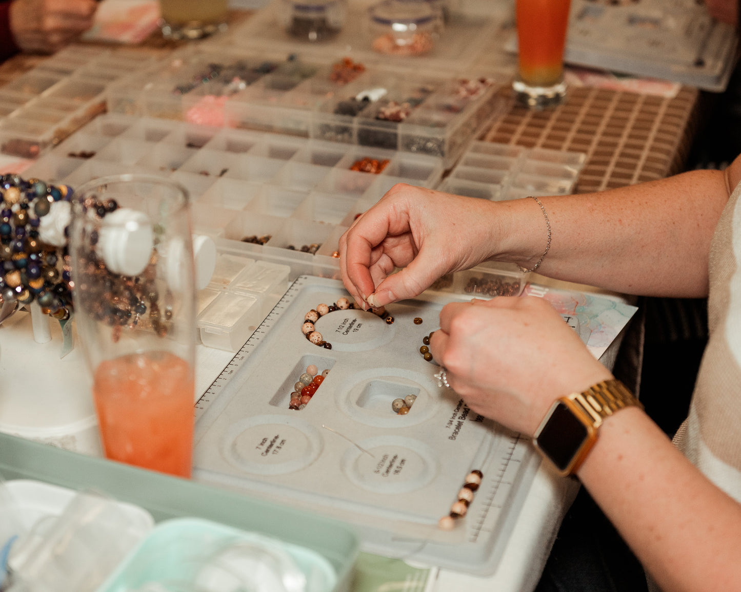 Person assembling jewelry at a table with various supplies and tools.