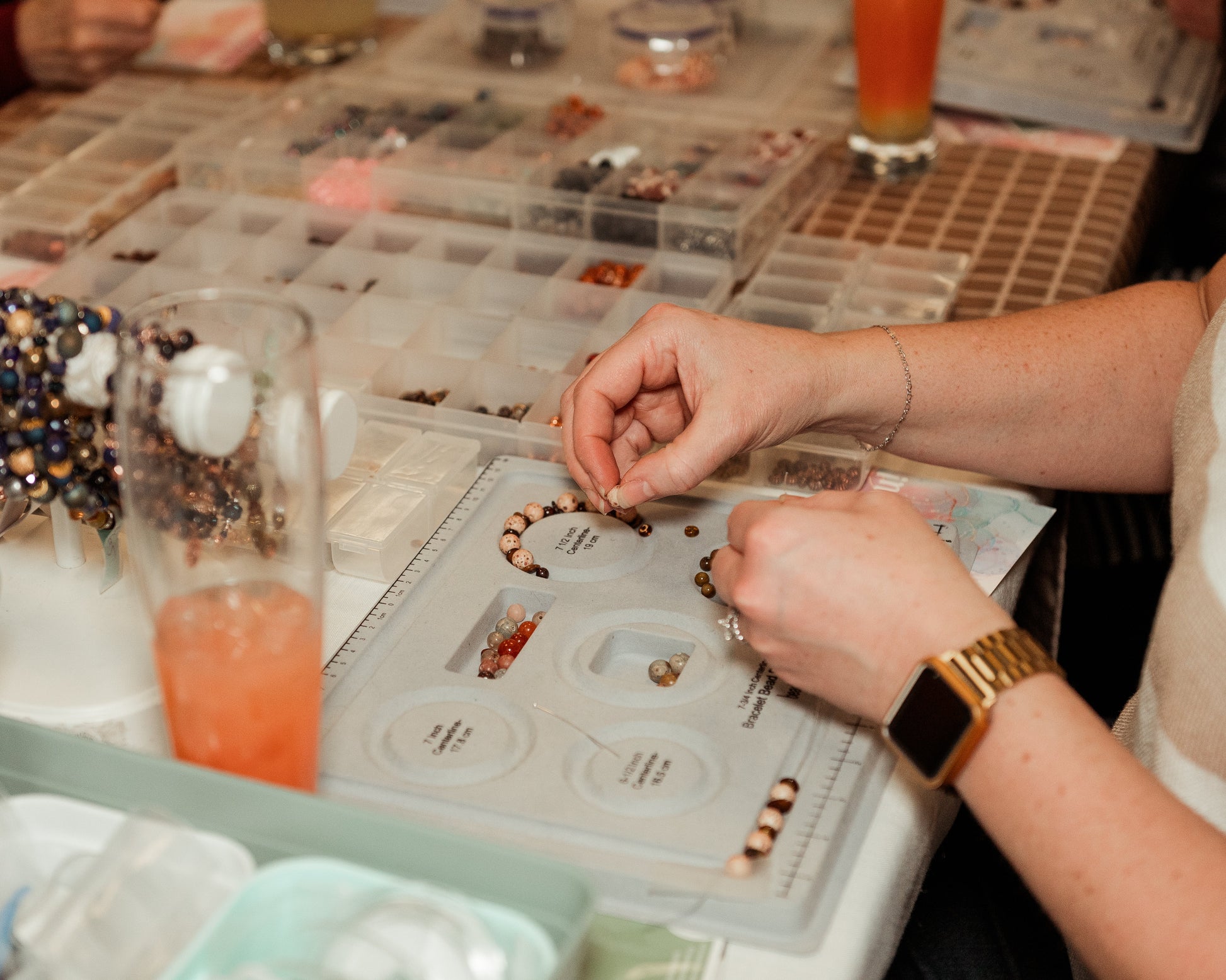 Person assembling jewelry at a table with various supplies and tools.