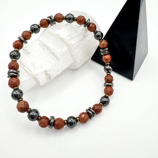 Grounded Power handmade men's hematite and goldstone bracelet with wavy hematite spacers styled on selenite crystal and black geometric display, strength and grounding jewelry by Blue Jeans and Pearls Regina Saskatchewan