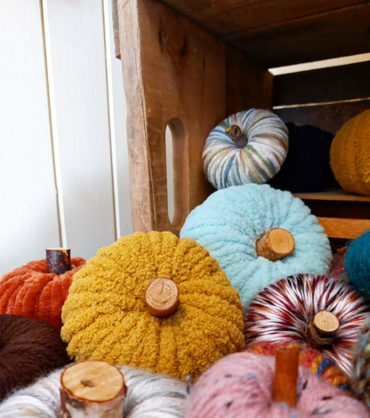 Handmade yarn pumpkins with natural wood branch stems in mustard, sky blue, burnt orange, pink and variegated yarns, piled in a rustic wooden crate, made at the DIY pumpkin decor workshop in Saskatchewan Beach