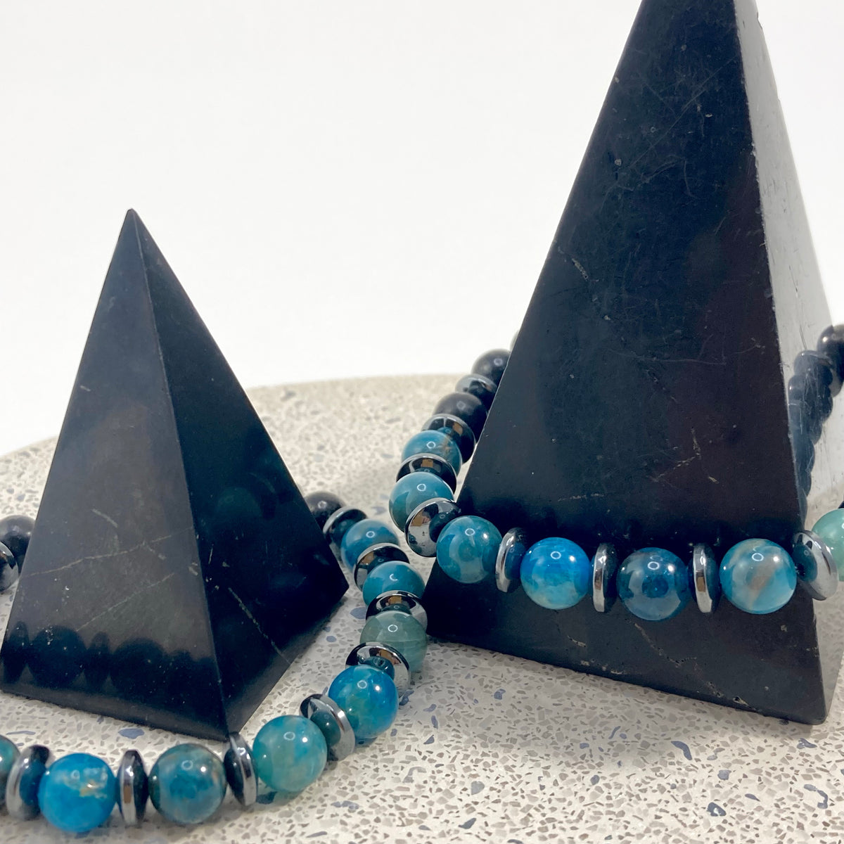 Men's Apatite, Shungite and Hematite handmade bracelets with vivid blue apatite 8mm beads, black shungite and hematite spacers draped on black pyramids on terrazzo, bold men's gemstone jewelry by Blue Jeans and Pearls Saskatchewan