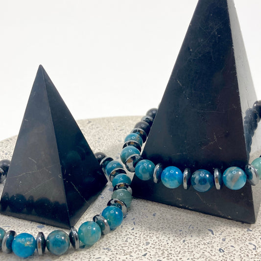 Men's Apatite, Shungite and Hematite handmade bracelets with vivid blue apatite 8mm beads, black shungite and hematite spacers draped on black pyramids on terrazzo, bold men's gemstone jewelry by Blue Jeans and Pearls Saskatchewan