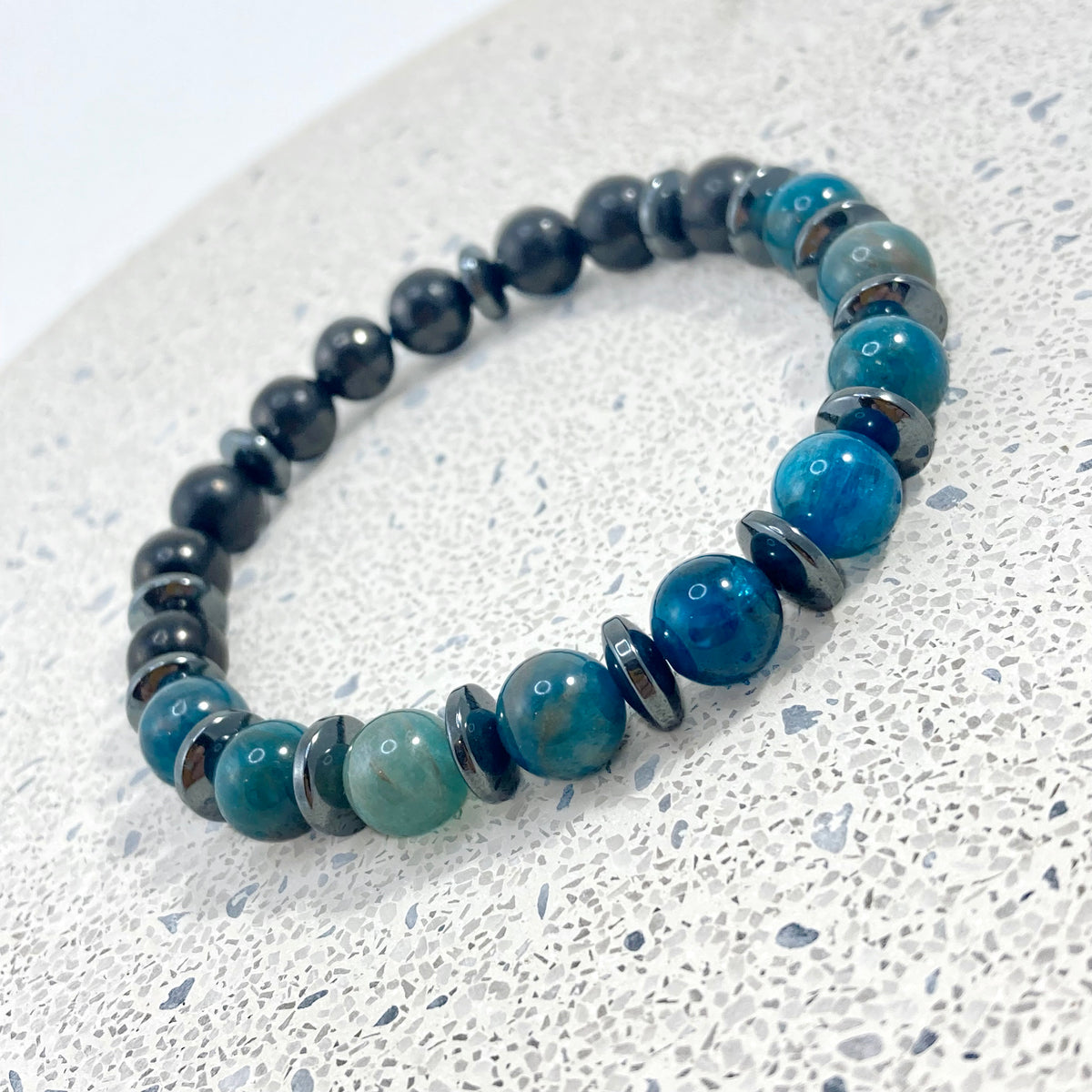 Men's Apatite, Shungite and Hematite handmade bracelet with blue apatite, matte black shungite beads and hematite saucer spacers on terrazzo, grounding men's gemstone jewelry handcrafted by Blue Jeans and Pearls Saskatchewan
