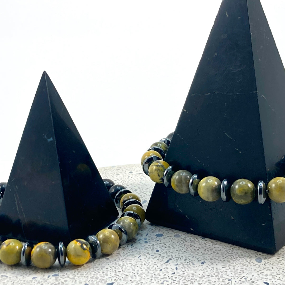 Men's Bumblebee Jasper, Shungite and Hematite handmade bracelets with yellow and black 8mm gemstone beads and silver hematite spacers draped on black pyramids on terrazzo, protective men's crystal jewelry by Blue Jeans and Pearls Saskatchewan