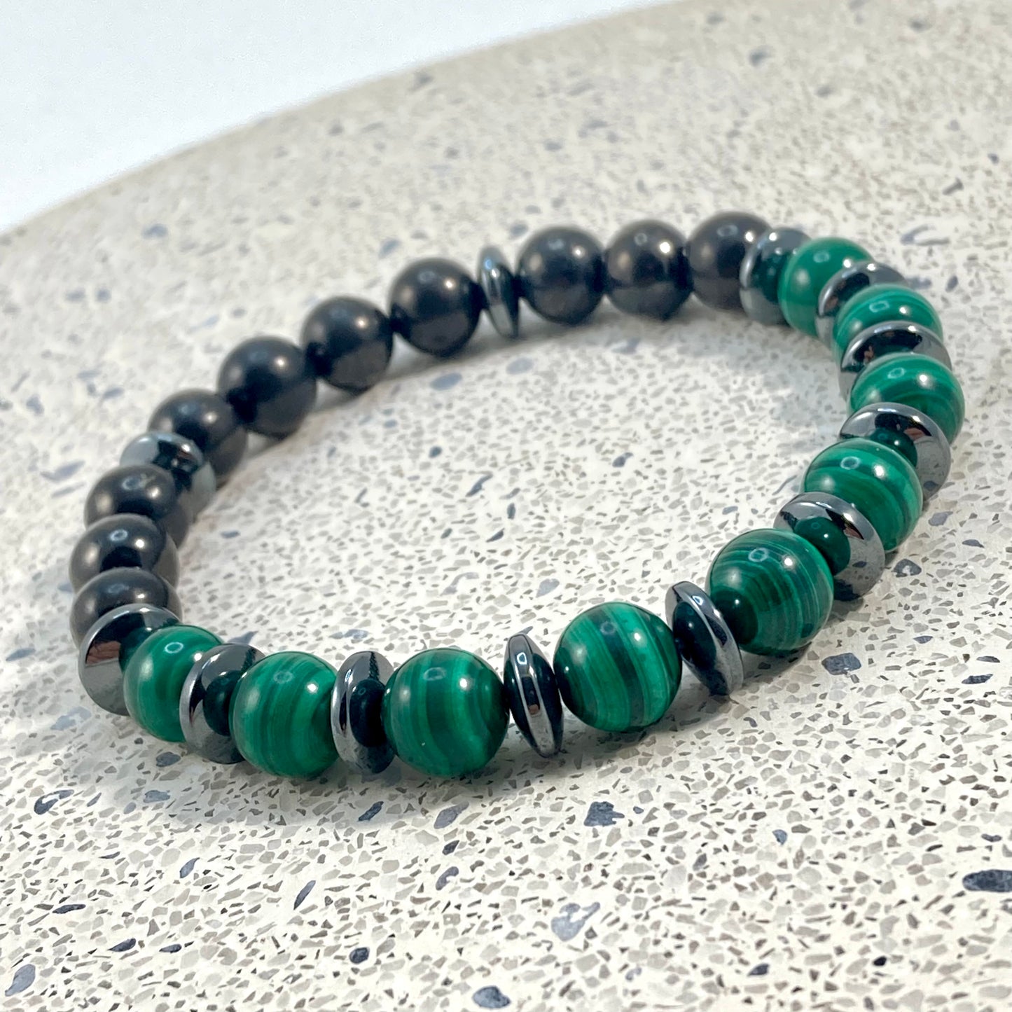 Men's Malachite, Shungite and Hematite handmade bracelet with banded green malachite, polished black shungite beads and hematite saucer spacers on terrazzo, bold men's gemstone jewelry handcrafted by Blue Jeans and Pearls Saskatchewan