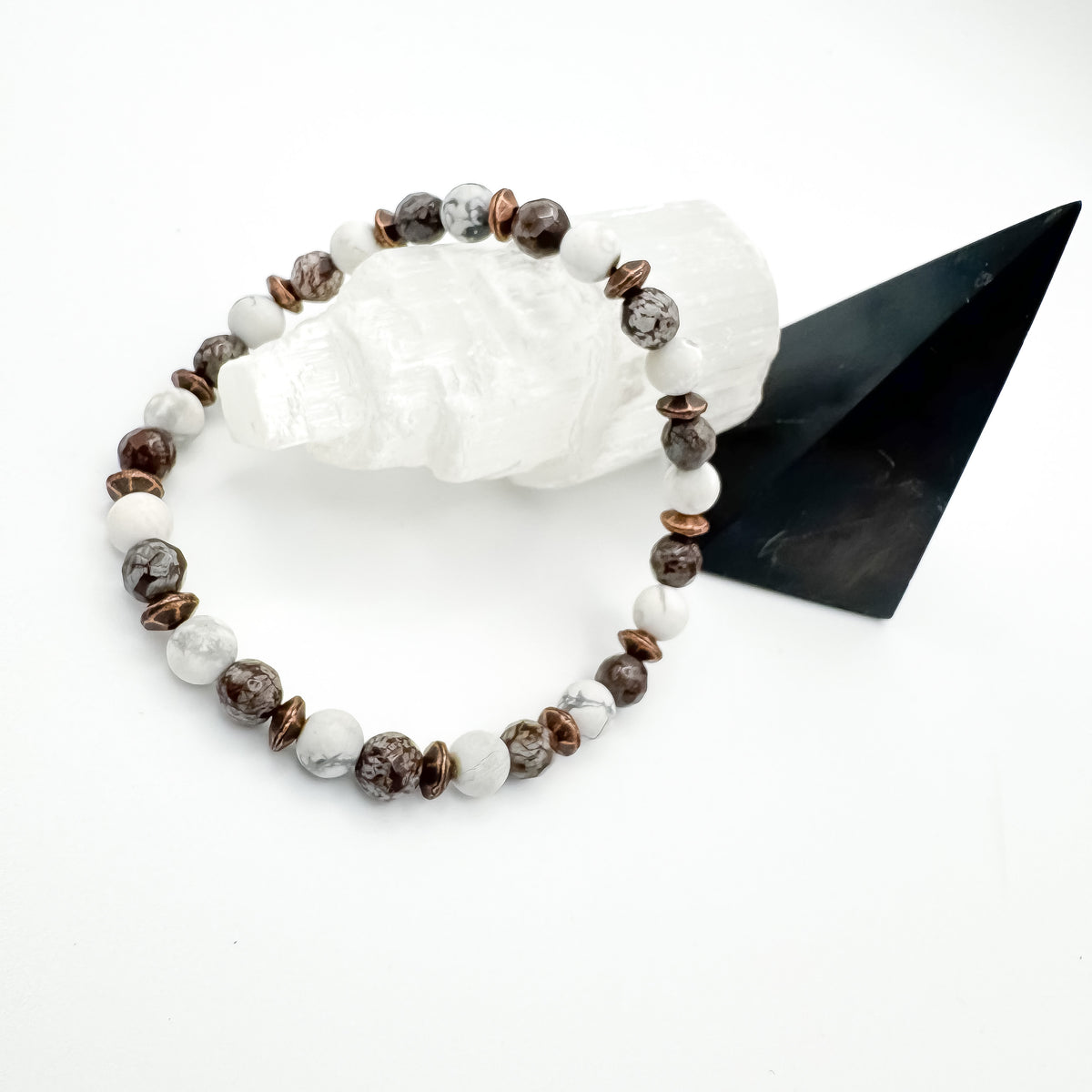 Men's Obsidian, Howlite and Copper handmade bracelet with faceted obsidian, white howlite beads and copper saucer spacers resting on raw selenite crystal beside black pyramid, grounding men's gemstone jewelry by Blue Jeans and Pearls Saskatchewan
