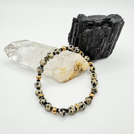 Rooted Light handmade bracelet with 6mm star cut dalmatian jasper, gold hematite square accents and gold round beads draped over clear quartz point beside raw black tourmaline crystal, grounding gemstone jewelry by Blue Jeans and Pearls Saskatchewan