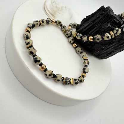 Rooted Light handmade star cut dalmatian jasper bracelet with gold round beads and gold hematite square accents on white pedestal, second bracelet draped on raw black tourmaline, close up of spotted gemstone jewelry by Blue Jeans and Pearls Saskatchewan