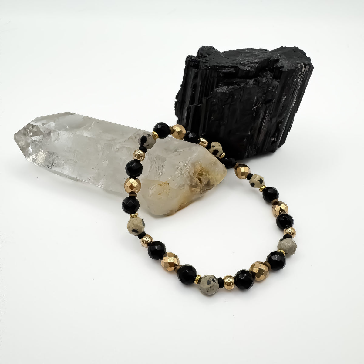 Sacred Flow handmade bracelet with dalmatian jasper, faceted black onyx and gold hematite beads draped over clear quartz point beside raw black tourmaline crystal, grounding gemstone jewelry by Blue Jeans and Pearls Saskatchewan