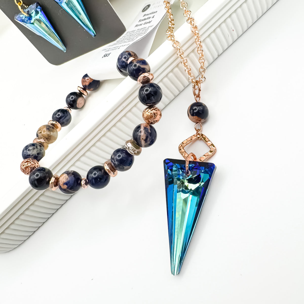 Seas and Sunsets Necklace with a 39mm Bermuda Blue crystal spike pendant, Brazilian sodalite bead and hammered rose gold connector on a rose gold plated chain, styled with a matching Brazilian sodalite and rose gold bracelet and Bermuda Blue spike earrings, by Blue Jeans and Pearls Saskatchewan