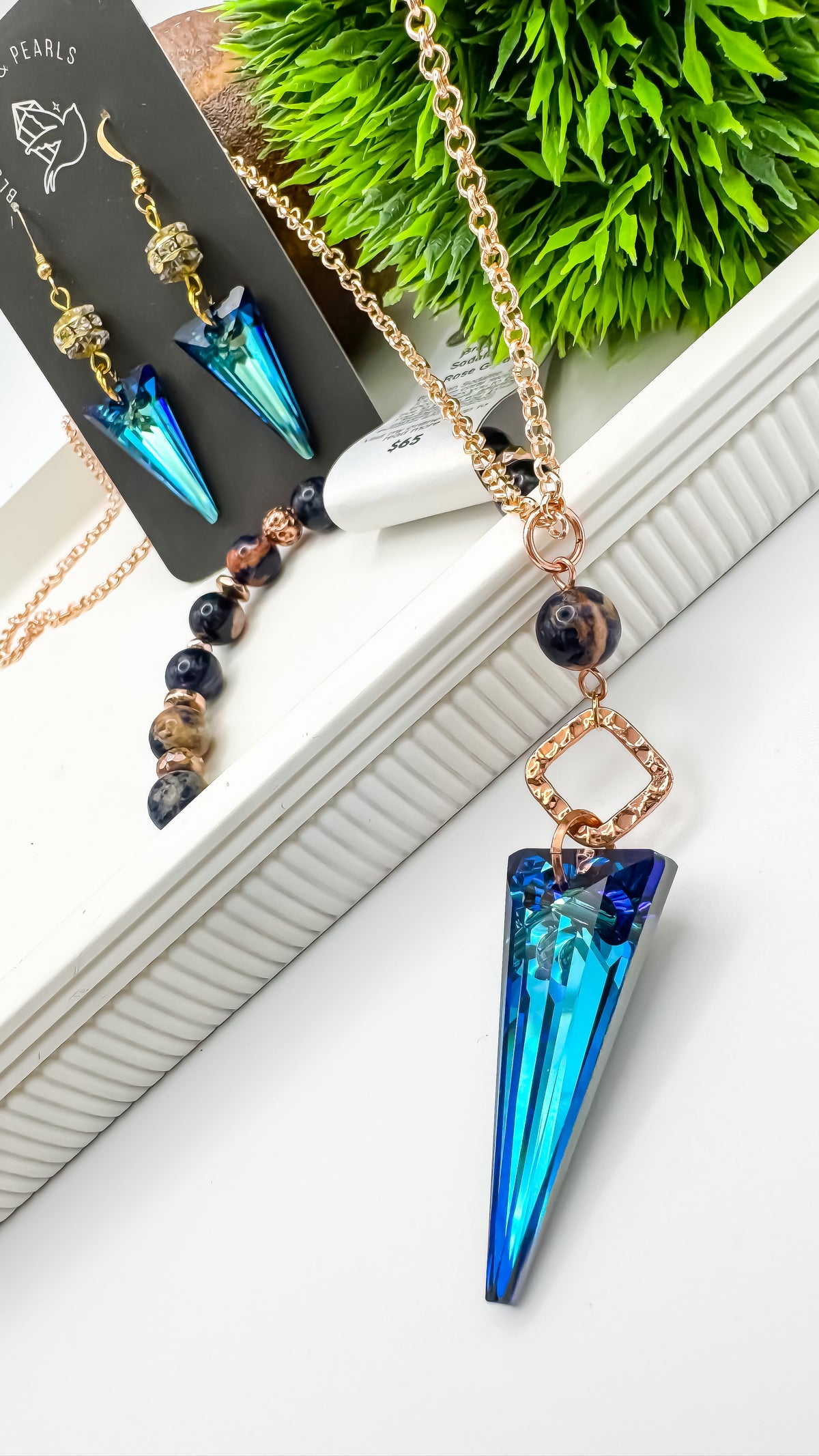 Seas and Sunsets Necklace with Bermuda Blue crystal spike pendant on a rose gold plated chain, styled with matching Bermuda Blue crystal spike drop earrings on a Blue Jeans and Pearls card and a Brazilian sodalite bracelet, by Blue Jeans and Pearls Saskatchewan