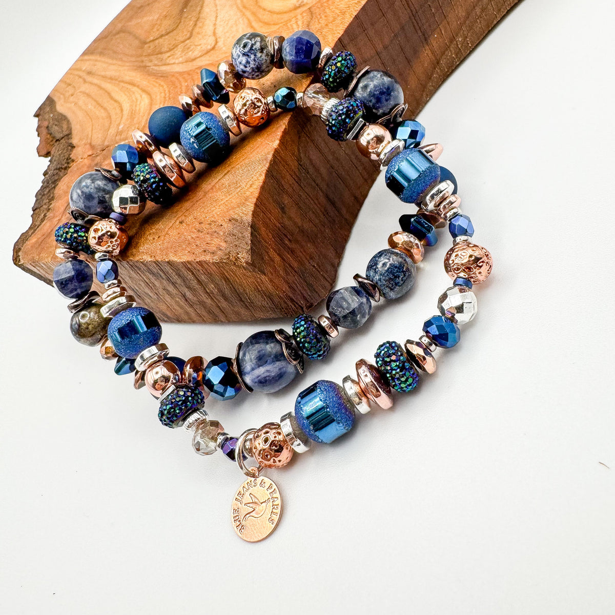 Silver Horizon and Living Skies handmade blue gemstone and mixed metal bracelet stack with rose gold Blue Jeans and Pearls charm displayed on natural wood slab, stackable prairie jewelry Saskatchewan