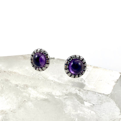 Amethyst stud earrings close up with 9mm round purple amethyst cabochons in scalloped stainless steel bezel settings on raw white crystal, natural gemstone earrings for sensitive ears by Blue Jeans and Pearls Saskatchewan