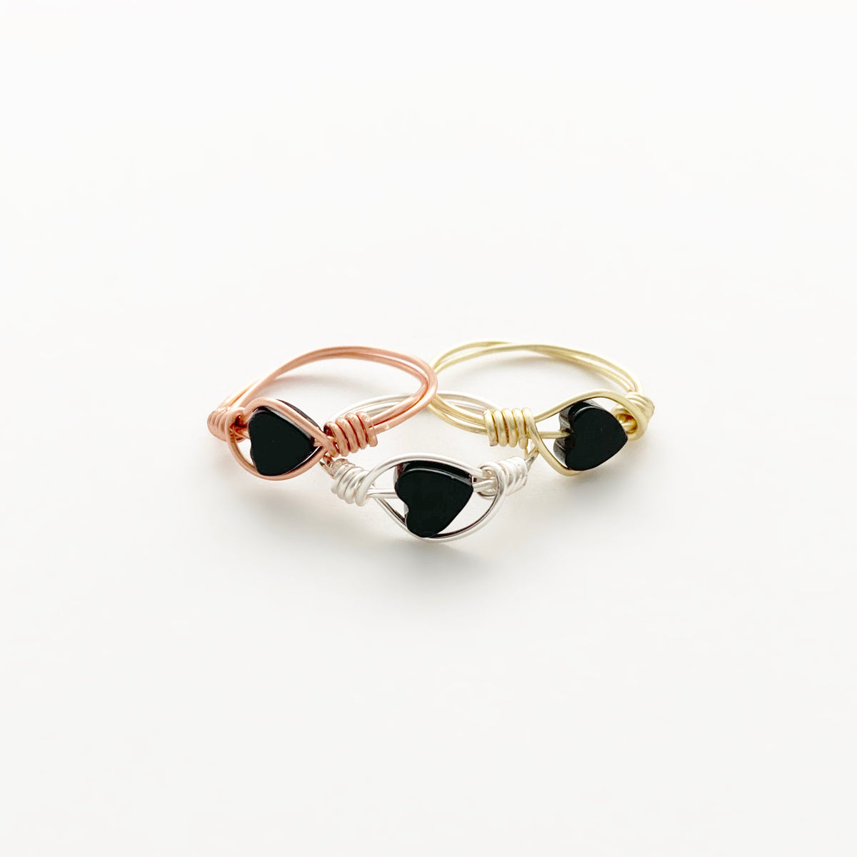 Three Black Onyx Heart wire-wrapped rings grouped together on a white background in rose gold, silver and gold finish copper wire, showing the coiled wrap detail, handmade gemstone heart rings by Blue Jeans and Pearls Saskatchewan