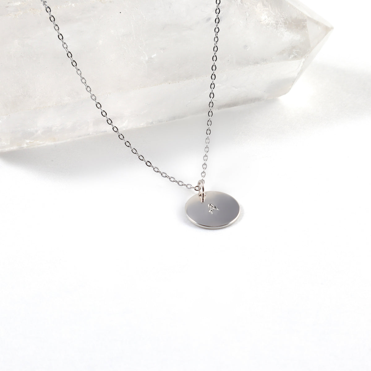 White Gold Round Hand Stamped Initial Necklace with an 11mm 14k white gold plated disc stamped with the letter A on a fine cable chain, styled against a clear quartz crystal point, personalized necklace by Blue Jeans and Pearls Saskatchewan